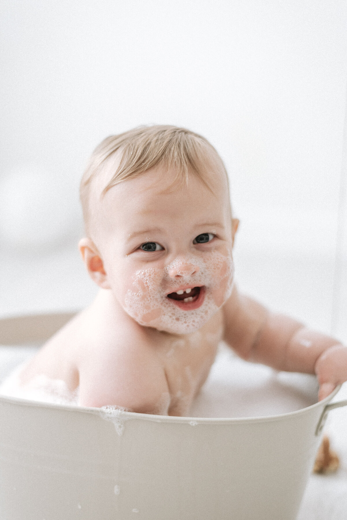 Baby smiling in a bath tub smiling with bubbles on his face in cake smash photoshoot