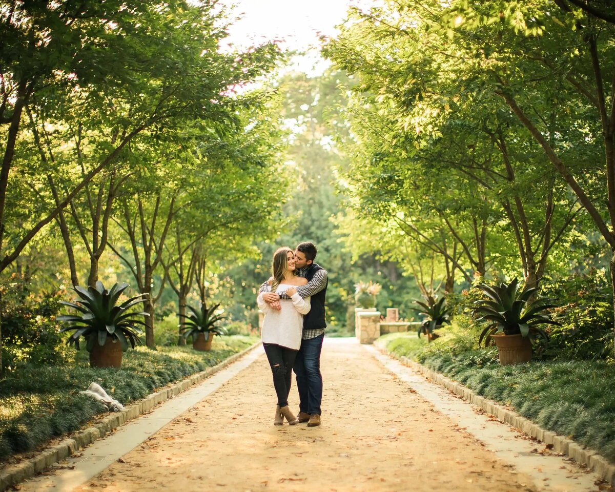 Couple kissing in the middle of a lush garden pathway, surrounded by greenery and sunlight