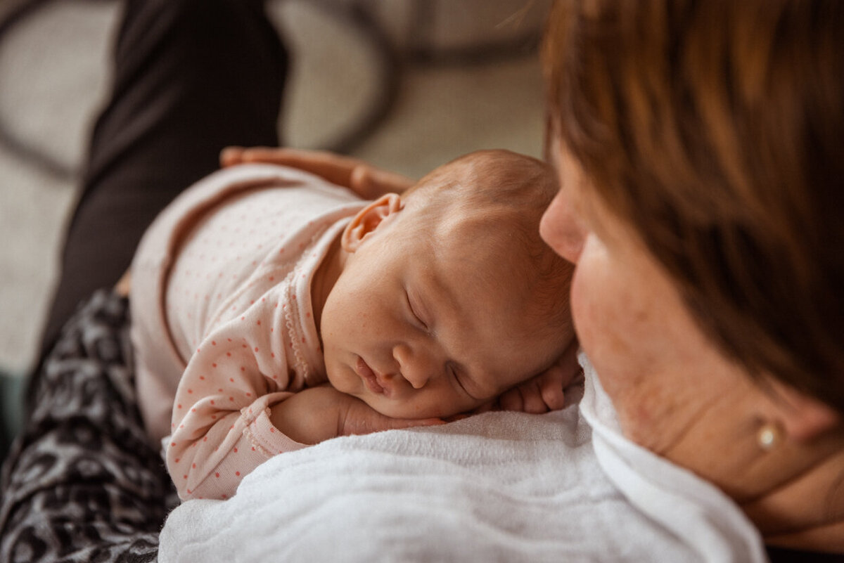 Livsstilsfoto tatt ovenfra og ned der baby sover på mormors bryst. Fokus er på babyens ansikt.