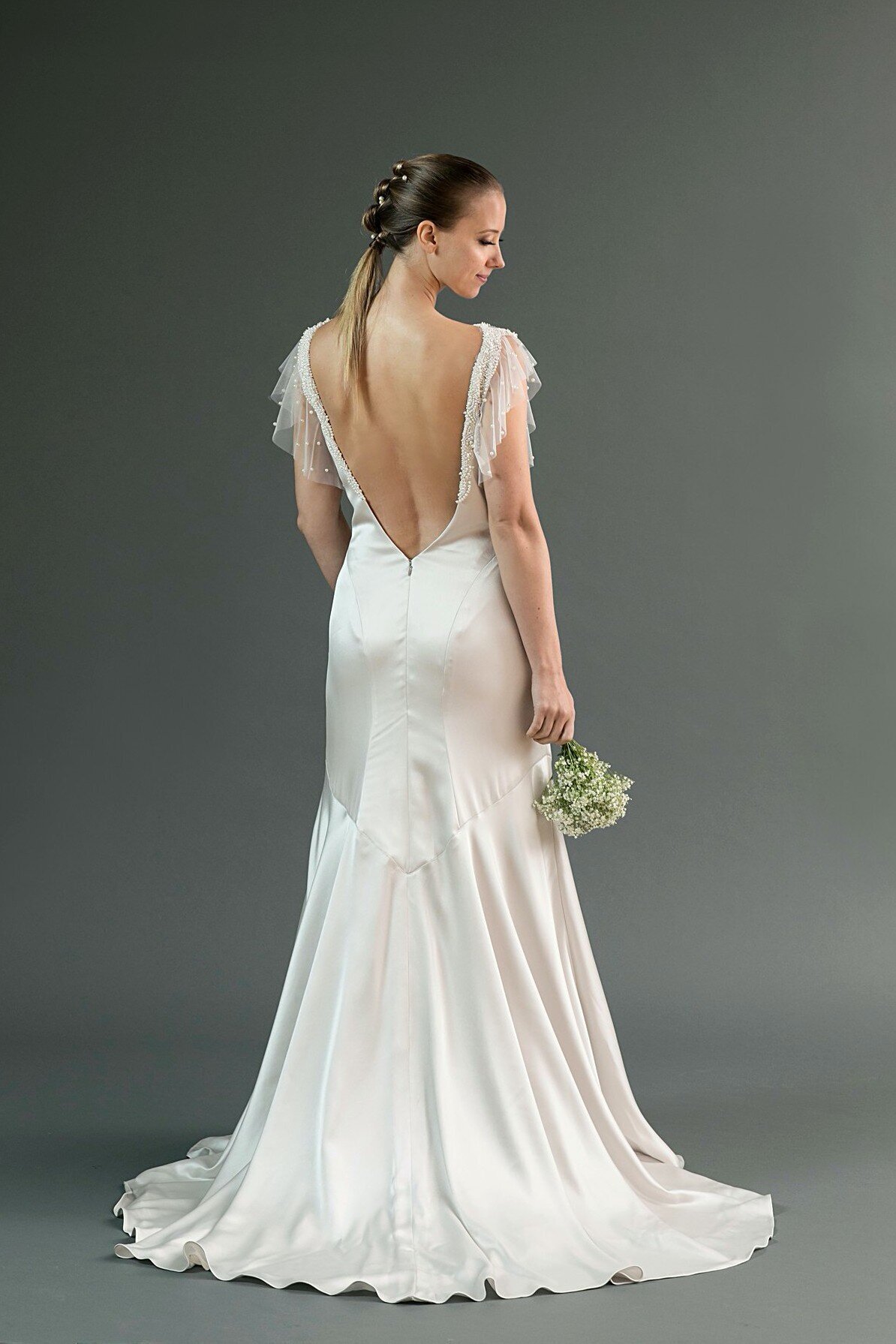 The low open-back wedding dress features a trumpet silhouette in a shiny charmeuse fabric. It's shown in silver, but available in white.
