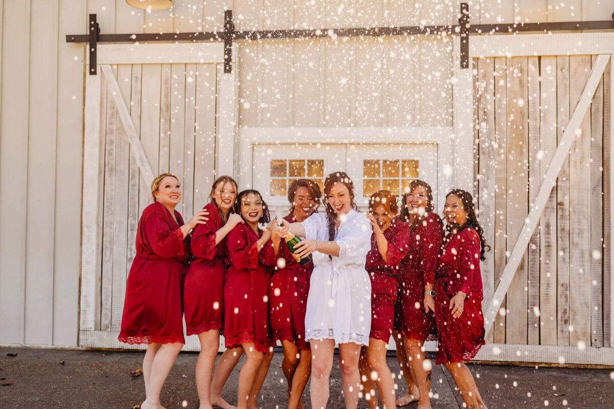Photo of a bride and her bridesmaids in roads popping a champagne bottle and laughing
