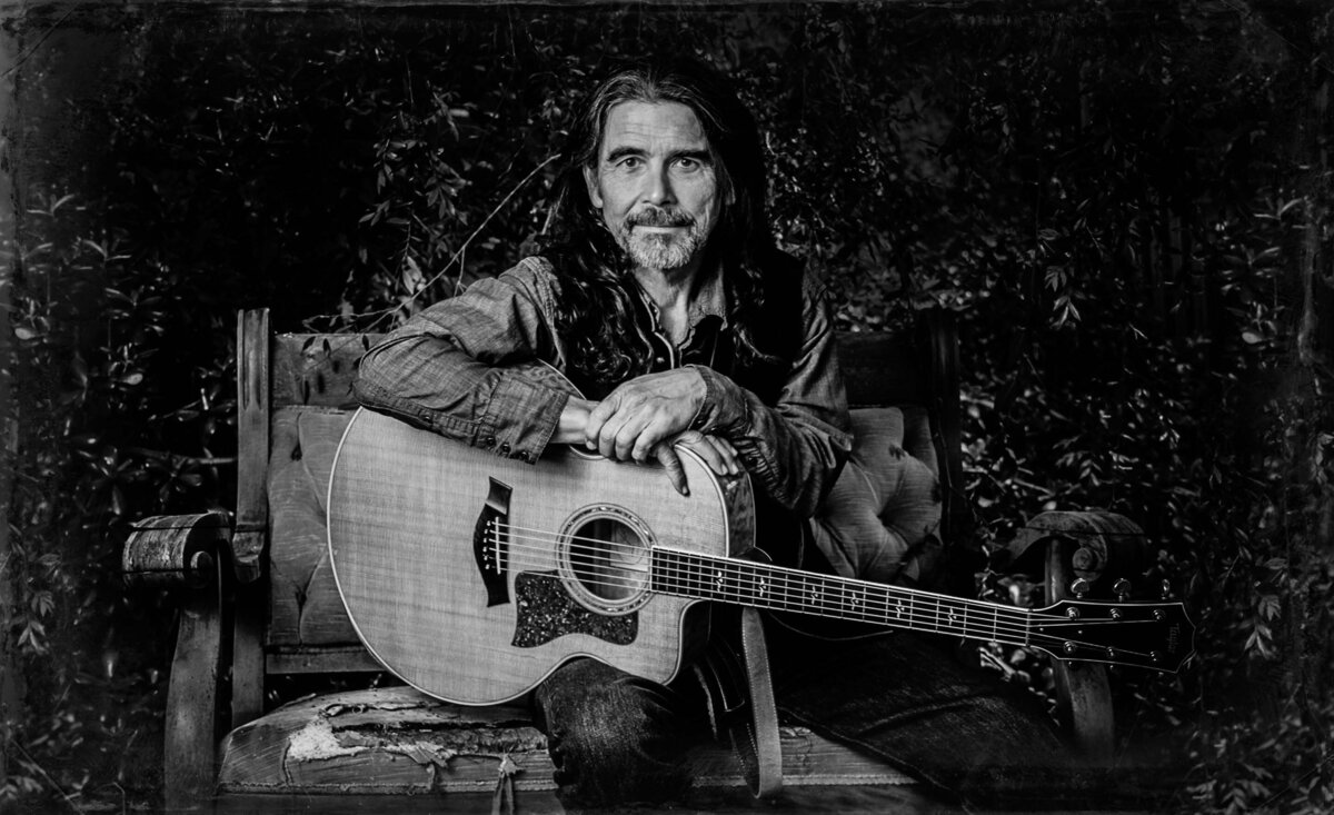 Country musician portrait black and white Jess Wayne sitting with arms crossed over guitar
