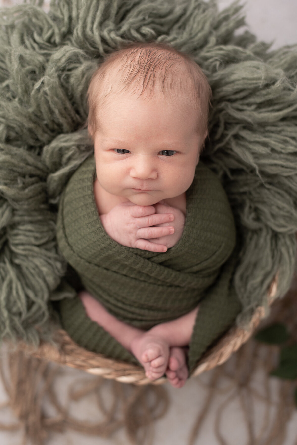 Newborn boy wrapped in green, looking at camera