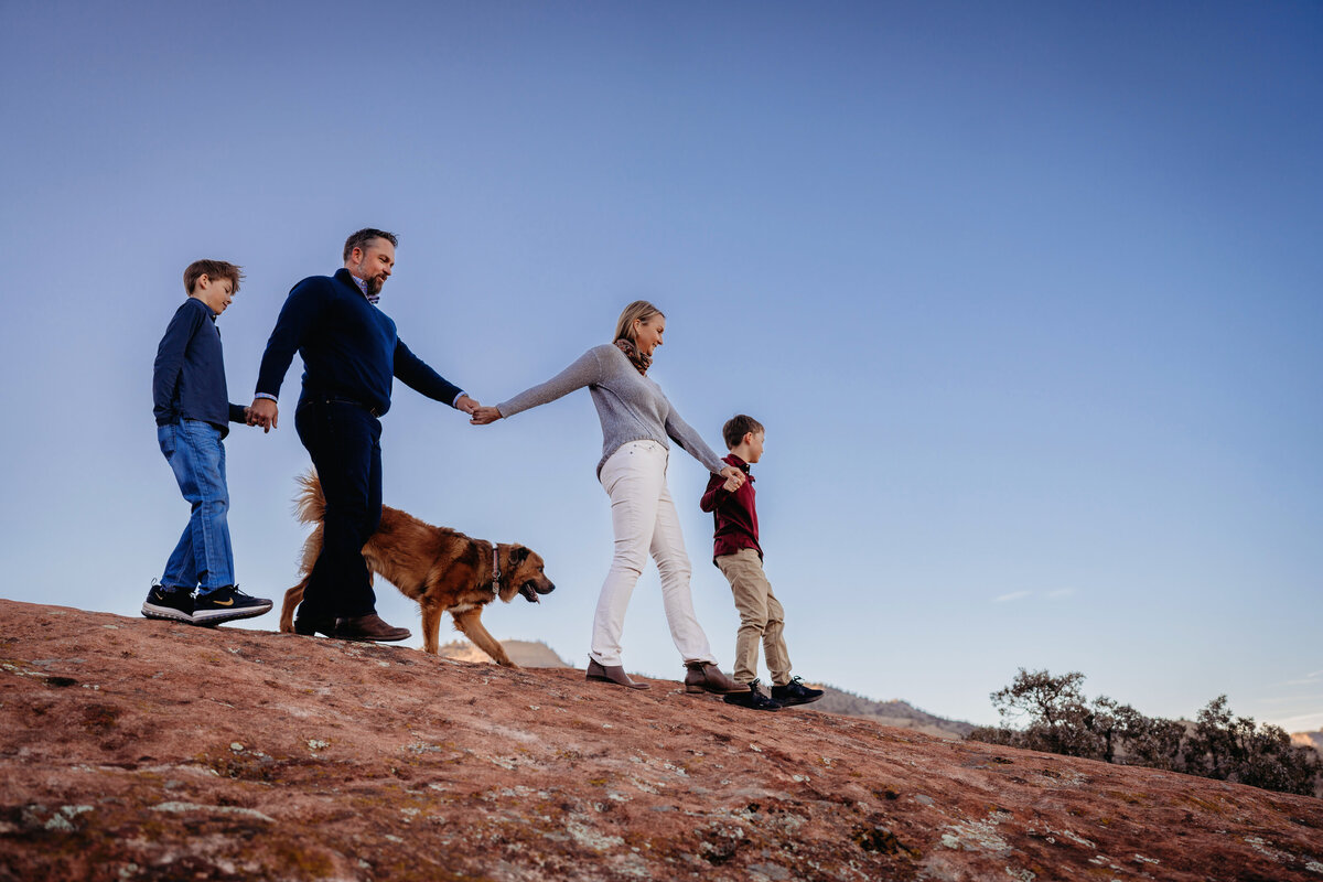 A family walks hand in hand together on a hike with their dog during their winter photoshoot in Morrison, Colorado