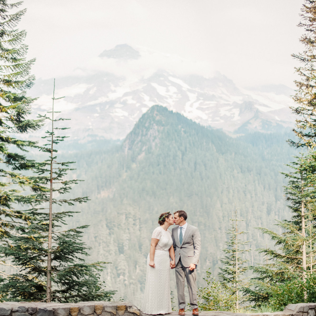 bride and groom stand on ledge of national park with mt rainier in background