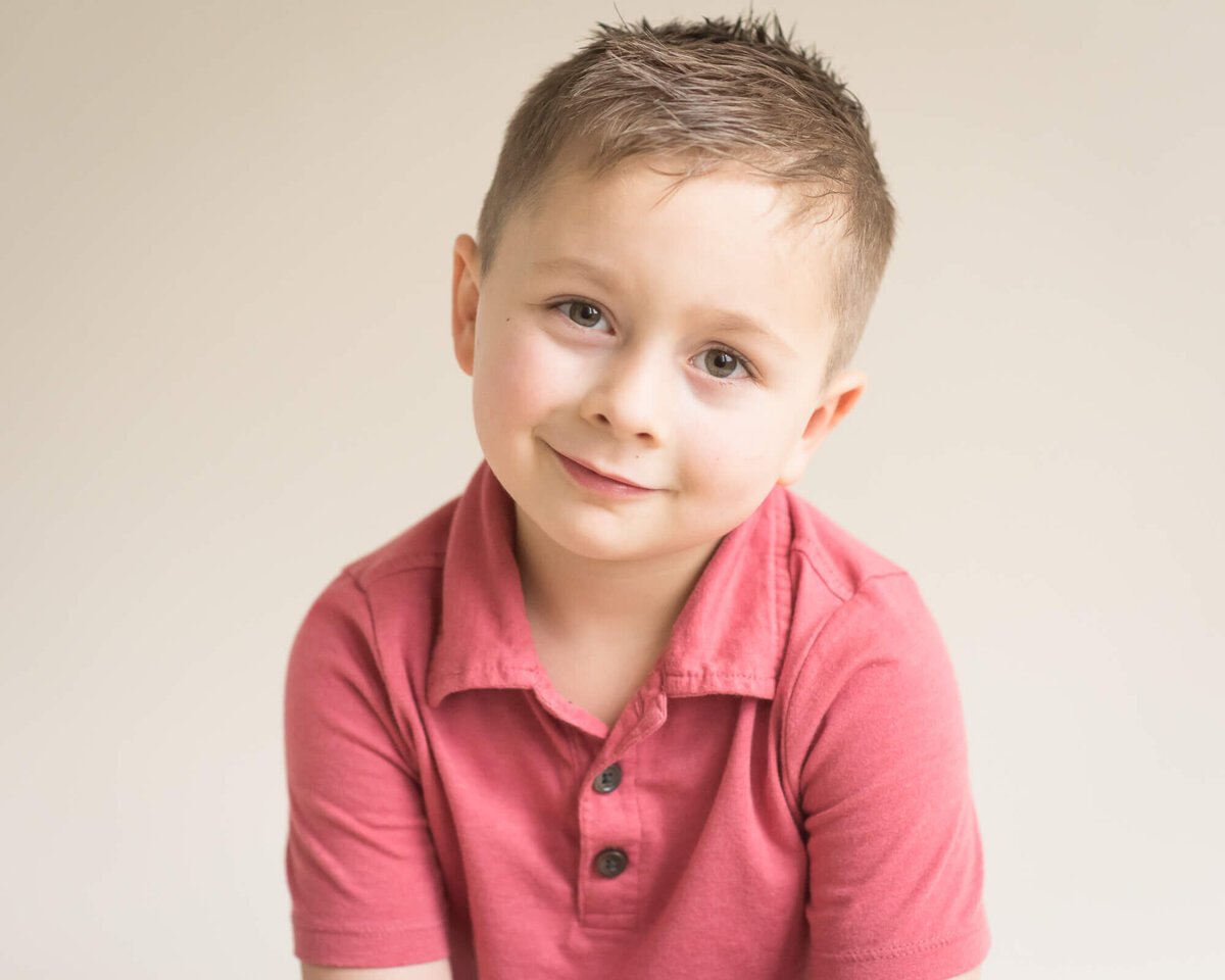 studio photo of a preschool-aged boy in a red shirt with a light colored background captured by Allison Amores Photography