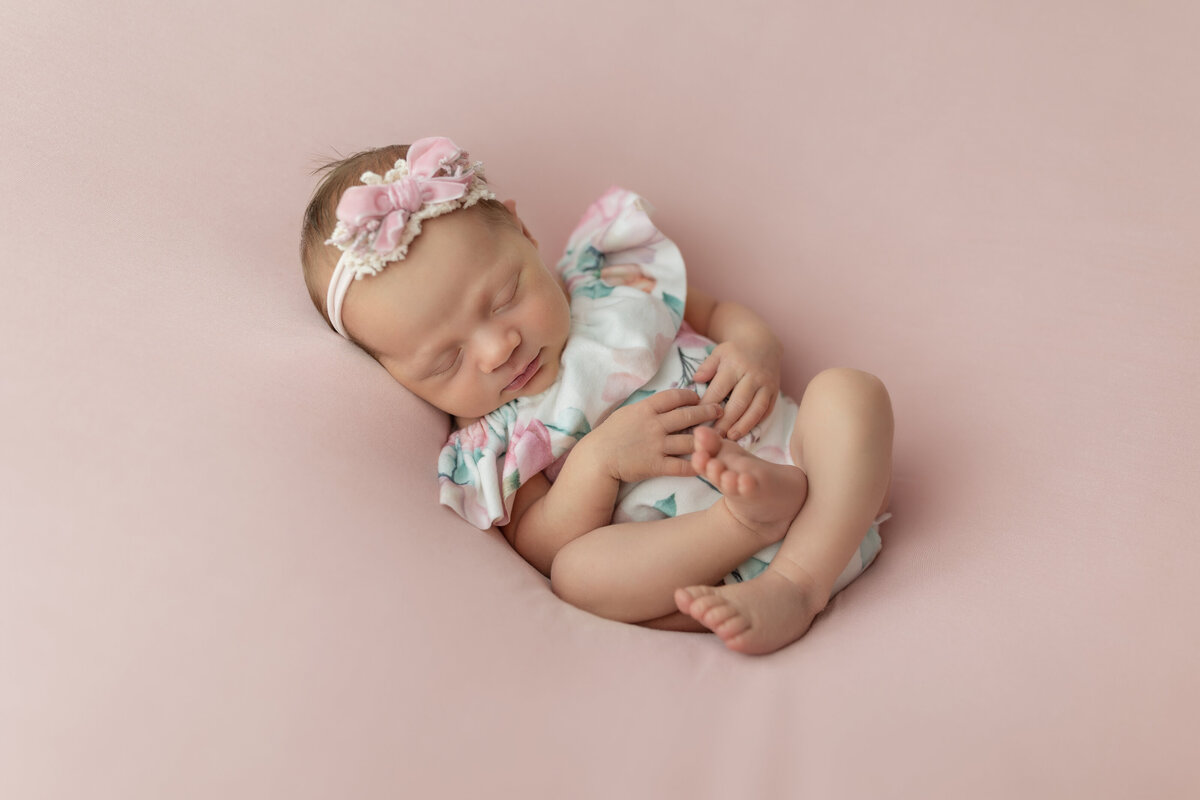 A newborn baby girl in a floral print dress sleeps on a studio pad in a NJ Newborn Photography studio