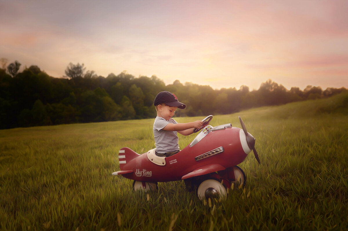 Little boy pretends to fly an antique toy plane in a field during Family Portraits in Asheville, NC.