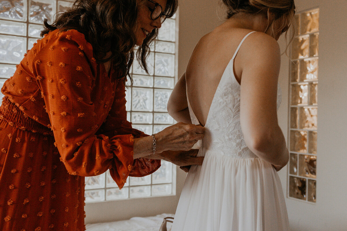 mom zipping up brides dress before ceremony