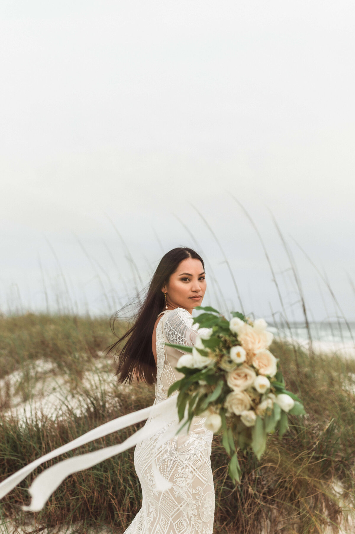 side portrait of asian bride in bridal dress and veil walks on beach path - taken by panama city fl photographer Brittney Stanley