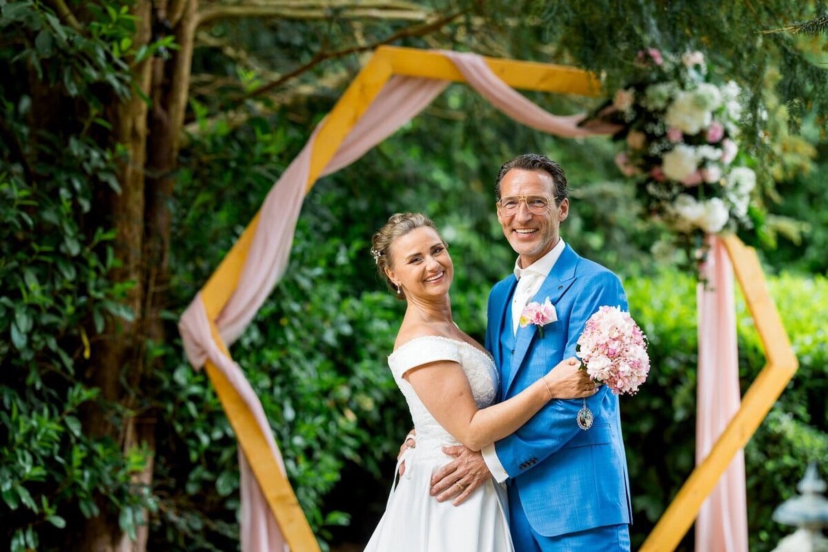 Bruidspaar poseert samen voor hun bruiloftsbackdrop, perfect georganiseerd door weddingplanner en ceremoniemeester