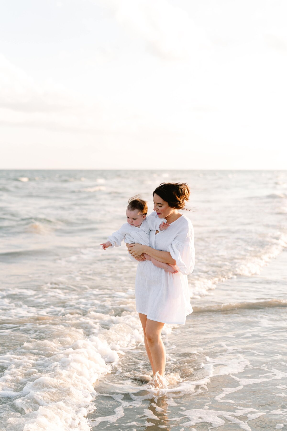 Young mother looking at waves holding baby