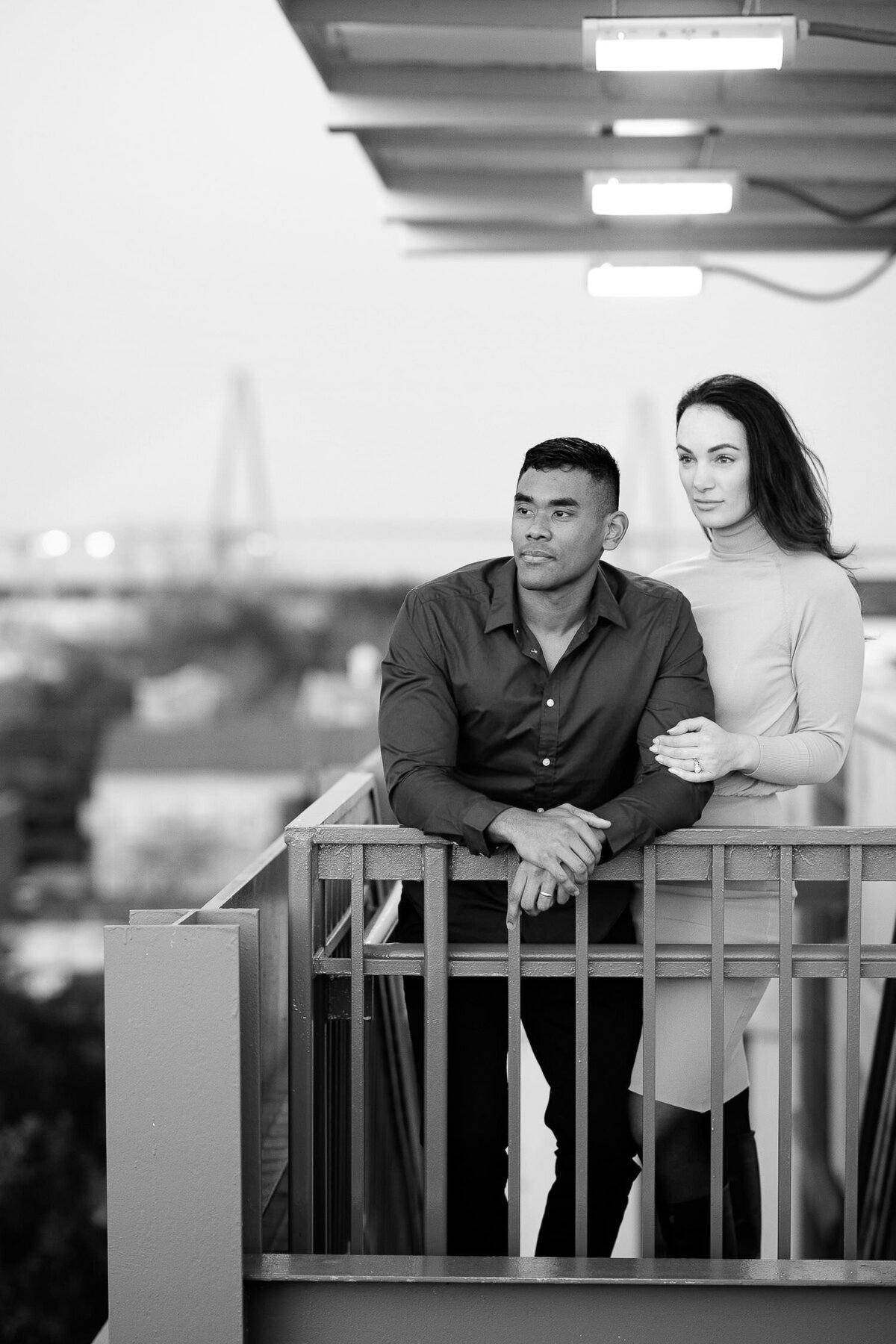 Parking garage engagement session. Couple looking from top of garage staircase with Charleston bride in background