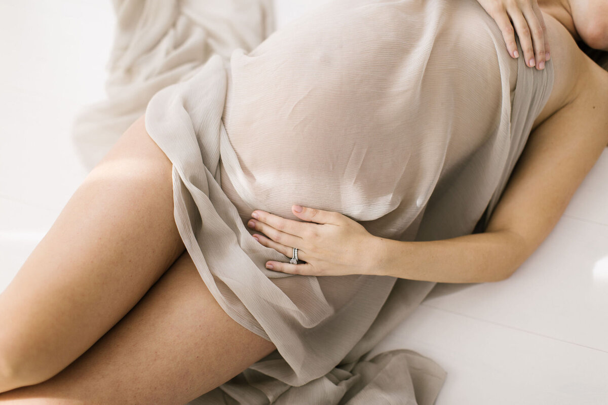 maternity photo of woman laying on floor with sheer tan fabric over belly