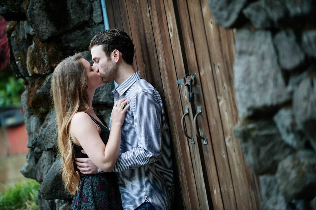 a couple kisses in front of a rustic wooden door