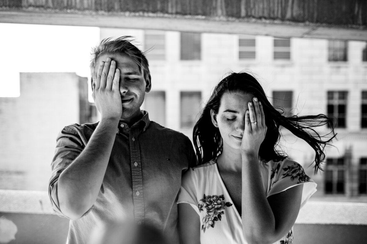 Black and White Engagement photo in downtown Toledo Ohio. The couple has a hand over their eye.  Photo By Adore Wedding Photography. Toledo Wedding Photographers
