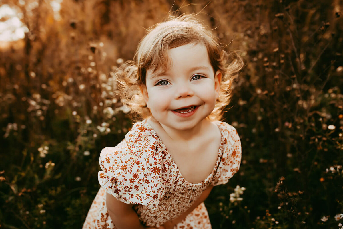 a beautiful smiling toddler leaning forward in a field of flowers