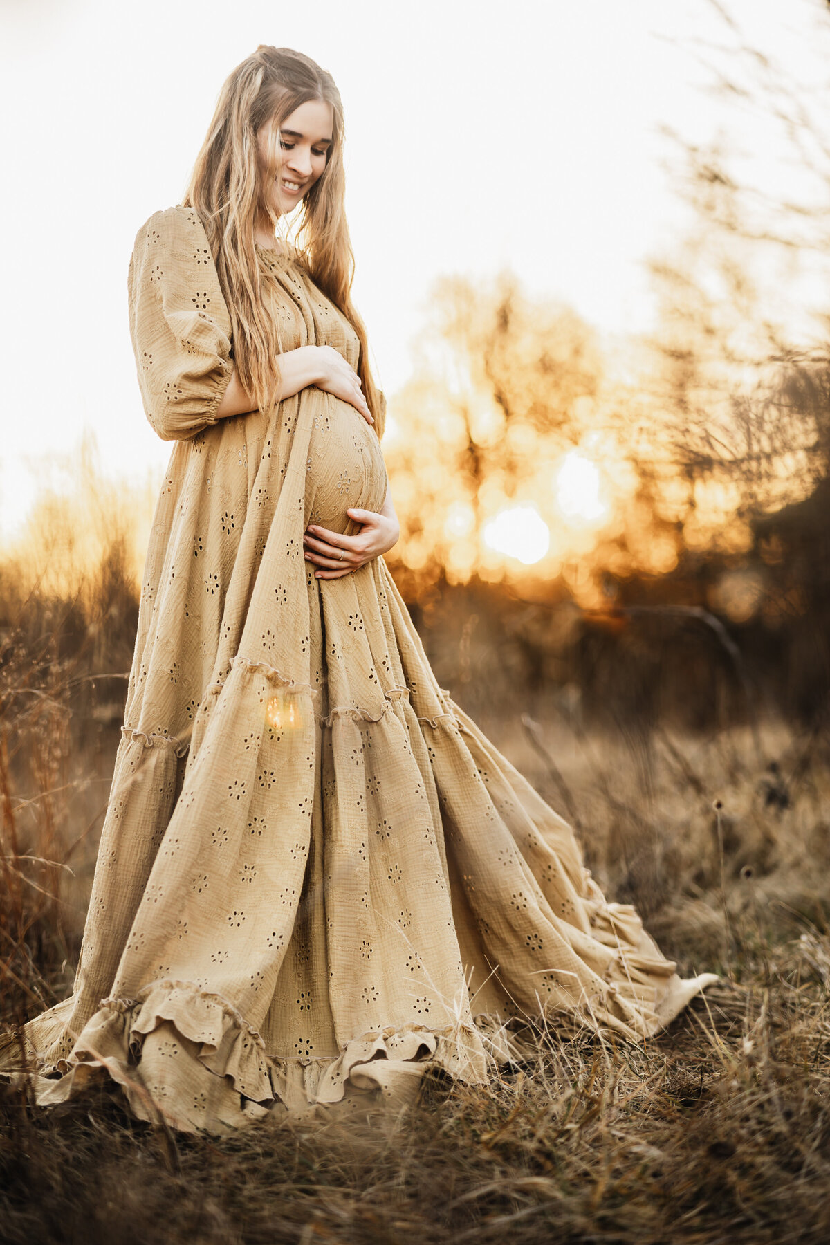 Pregnant mother embracing her belly in a beautiful camel colored eyelet gown at sunset in Harrisburg