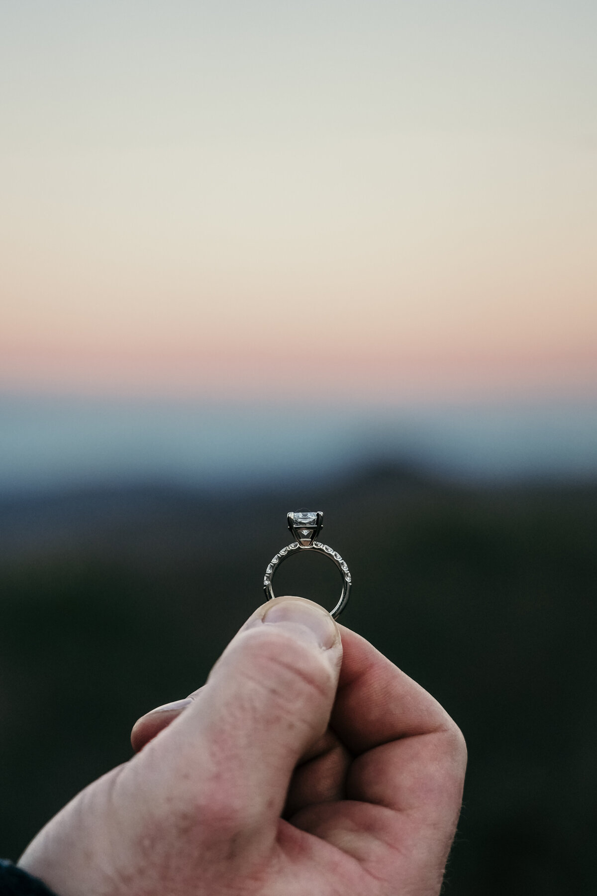 engagement ring held up with the mountains faded in the background