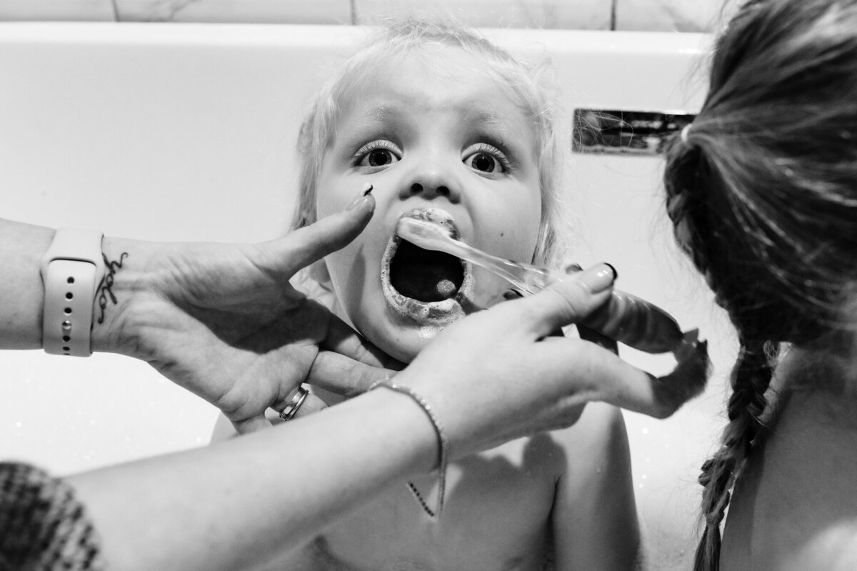 Little girl having her teeth brushed during at home family photoshoot
