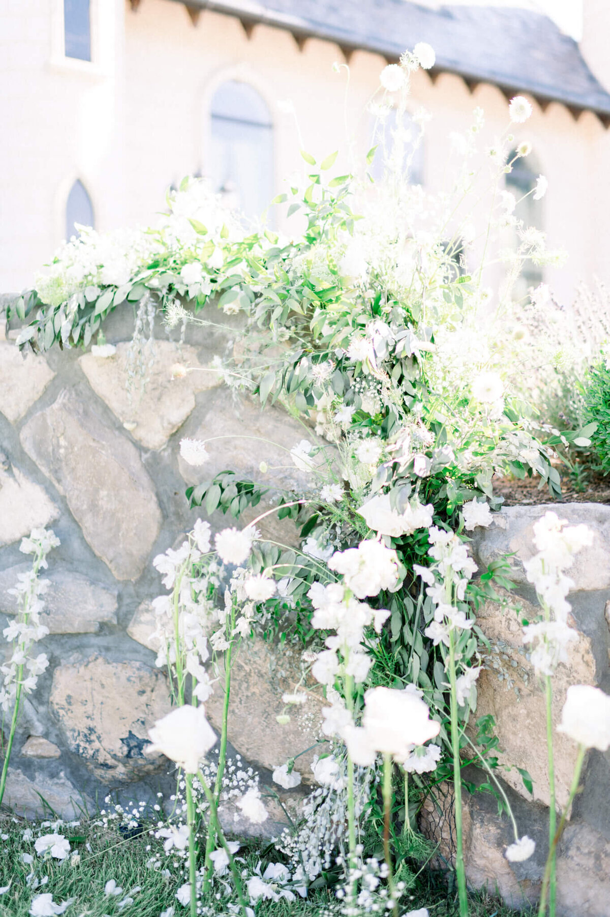 white and green flowers along rock wall with castle wedding venue in the background