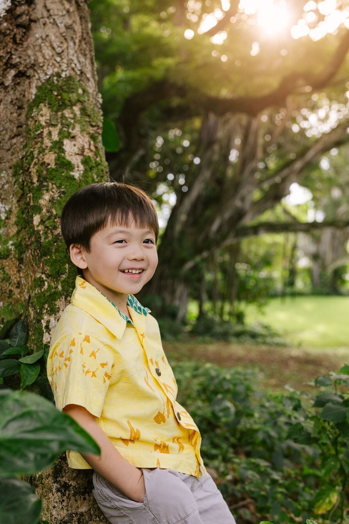boy leans against tree and laughs with forest behind