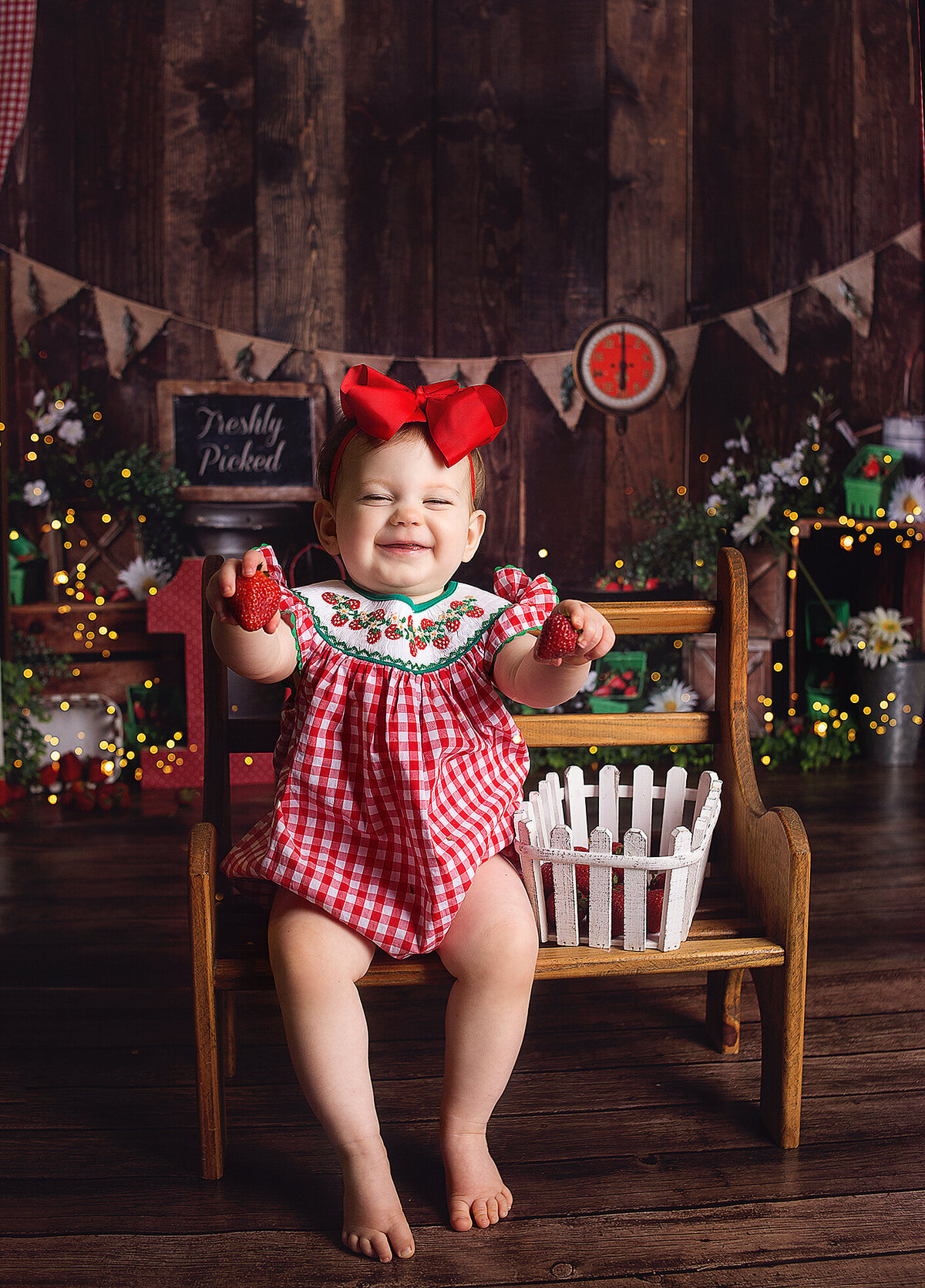 Little girl sitting on wood bench with red bow during cake smash photoshoot in Franklin Tennessee photography studio