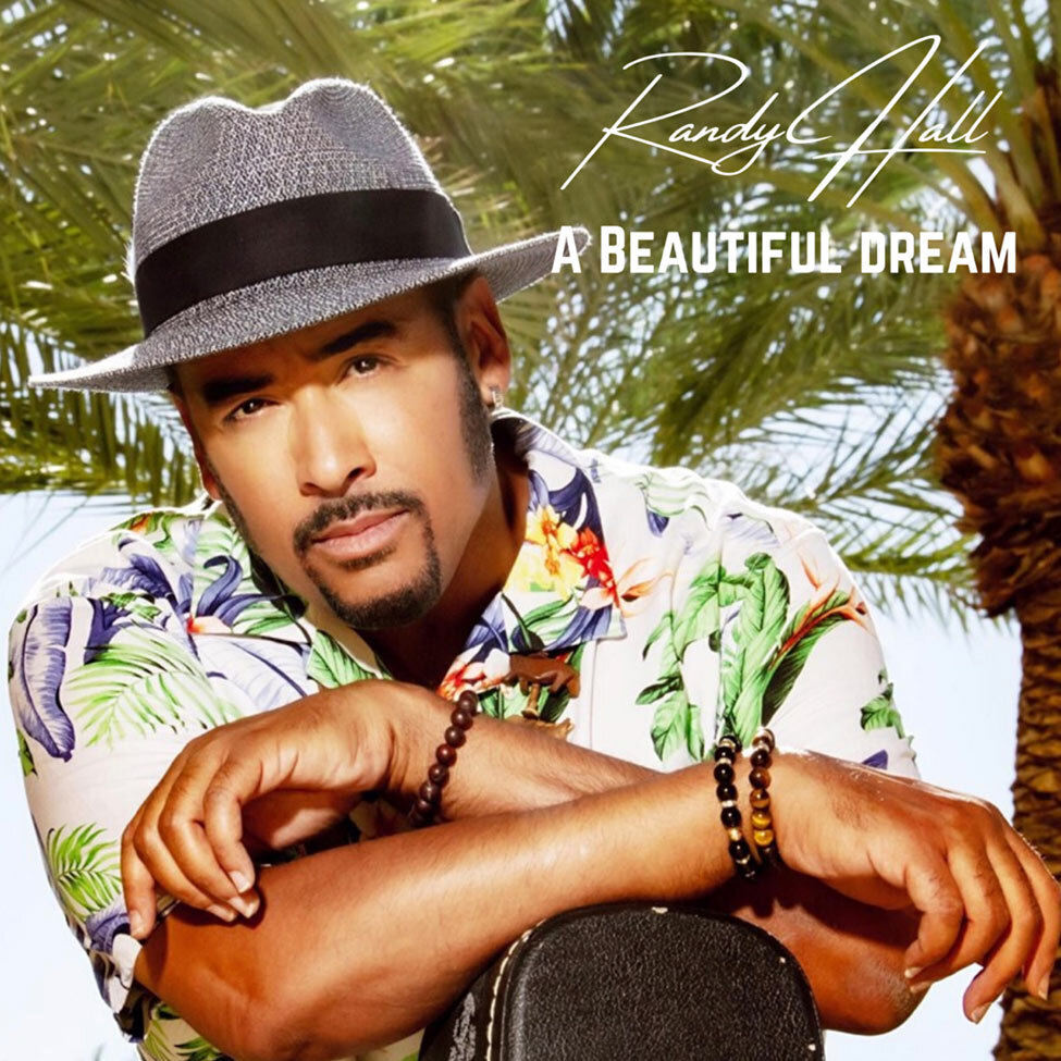 Single Cover Title A Beautiful Dream Artist Randy Hall wearing grey fedora with black trim hawaiian shirt leaning on upright guitar case palm tree behind him