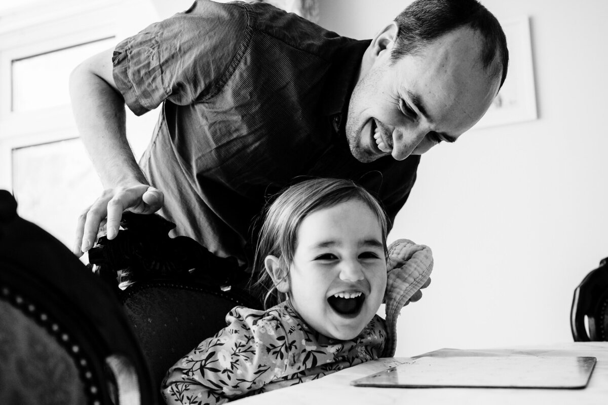 Dad laughing with daughter at dining table at home family photoshoot