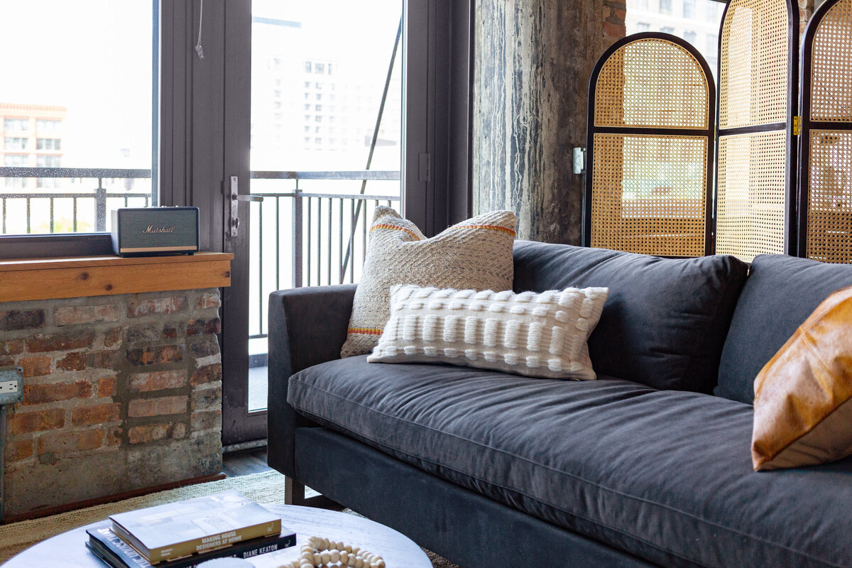 Industrial loft featuring brick walls and concrete columns with blue velvet sofa, arched cane divider screen