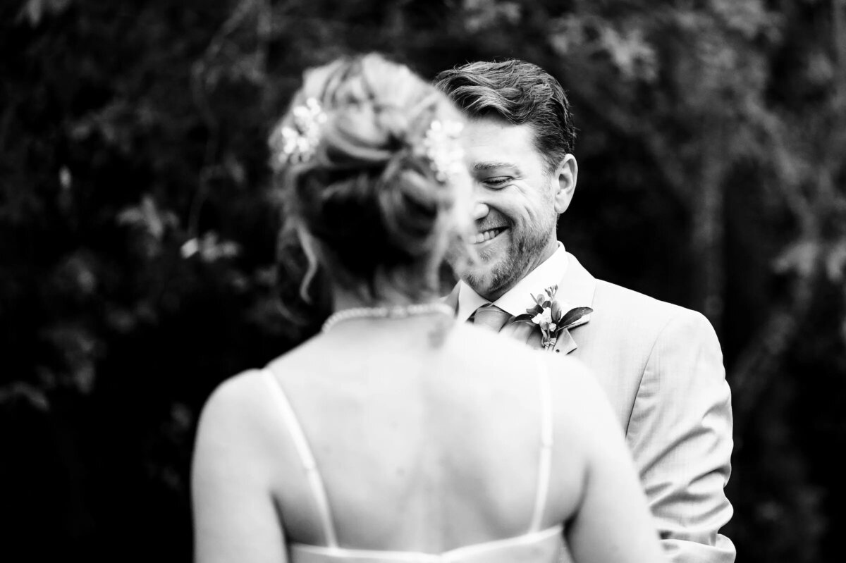 A tender moment in black and white, with a groom in a beige suit smiling at his bride from over her shoulder.