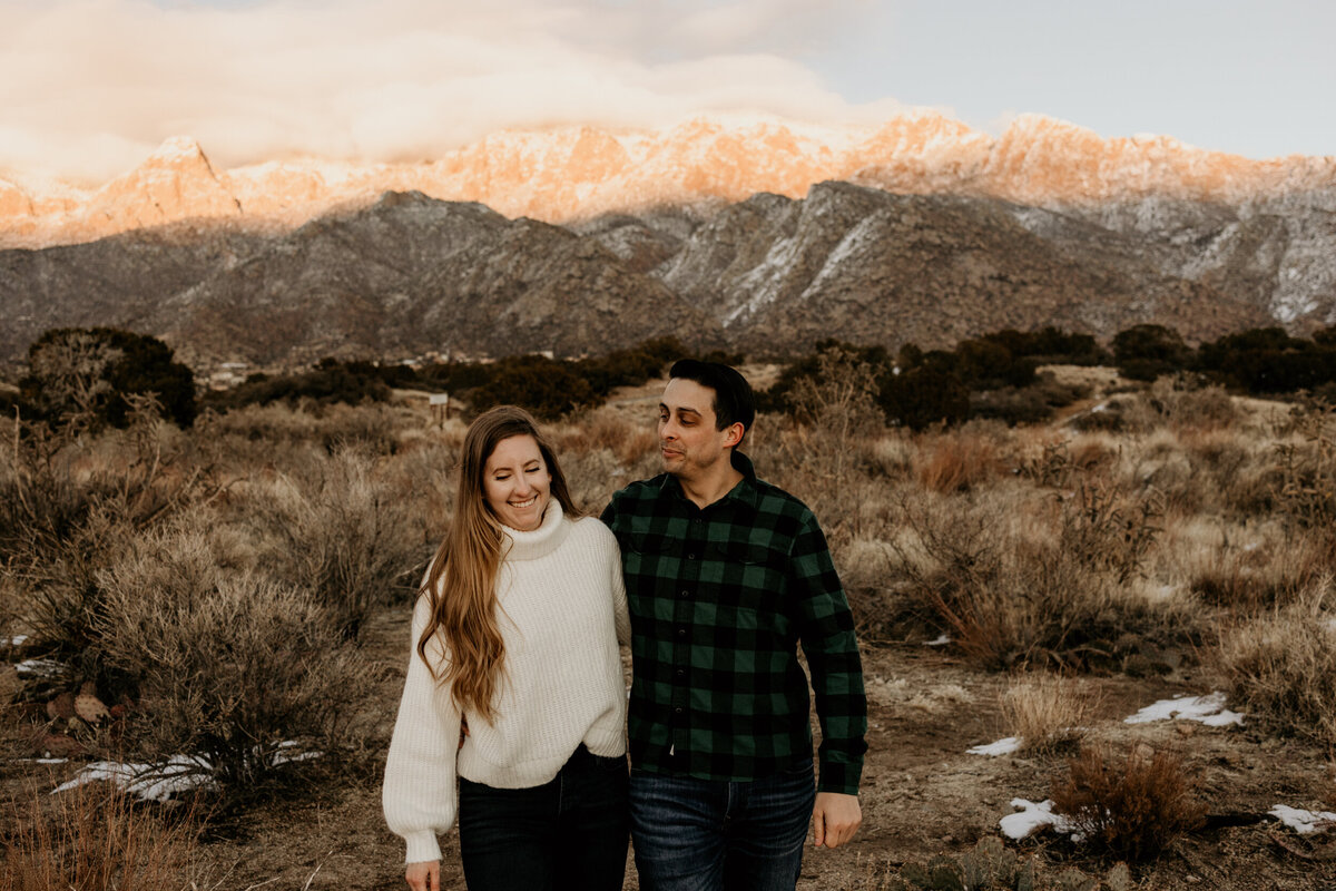 engaged couple walking in the New Mexico desert with a snowy mountain behind them