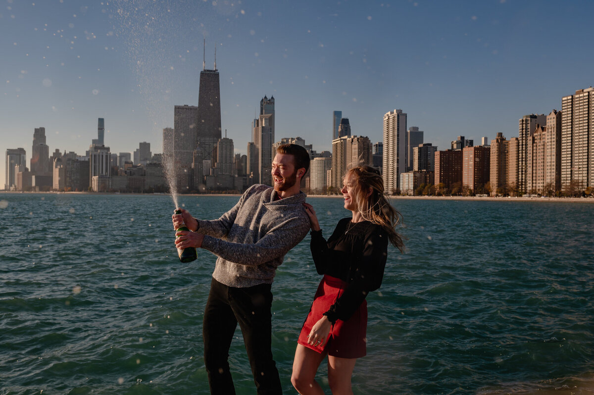 A couple spray a bottle of champagne in front of the Chicago skyline