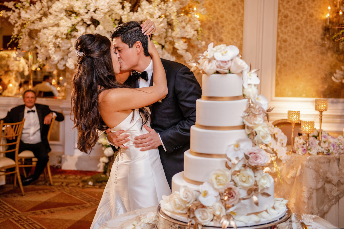 photo of bride and groom kissing behind wedding cake during wedding reception at The Garden City Hotel