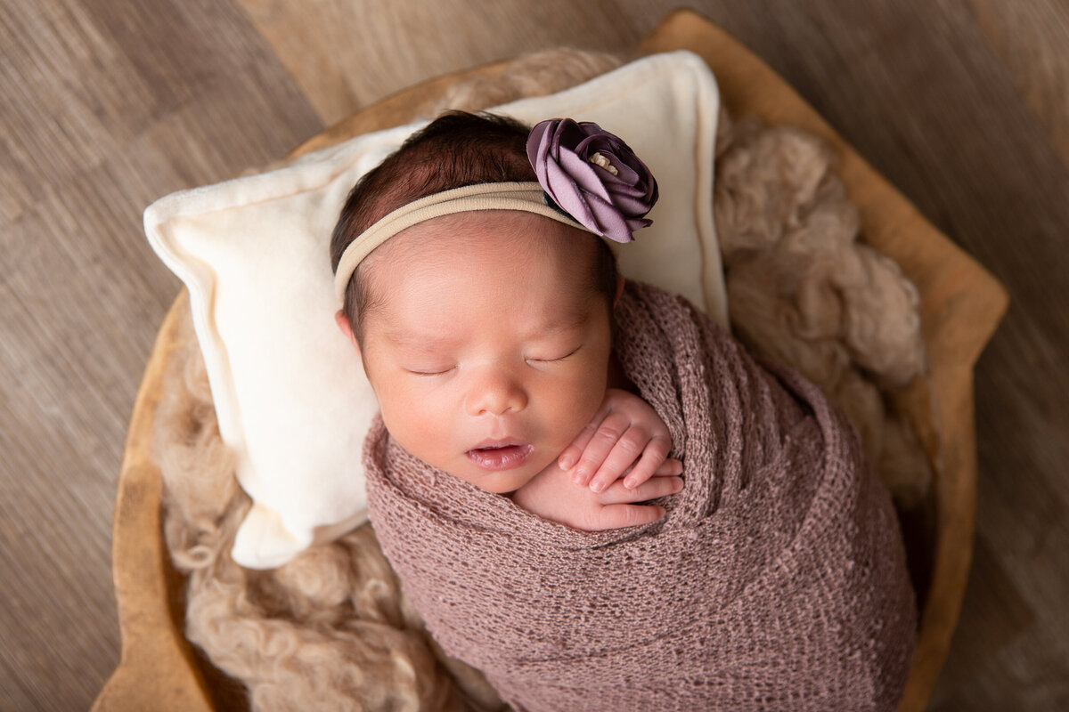 Mauve wrapped newborn in a carved wooden bowl