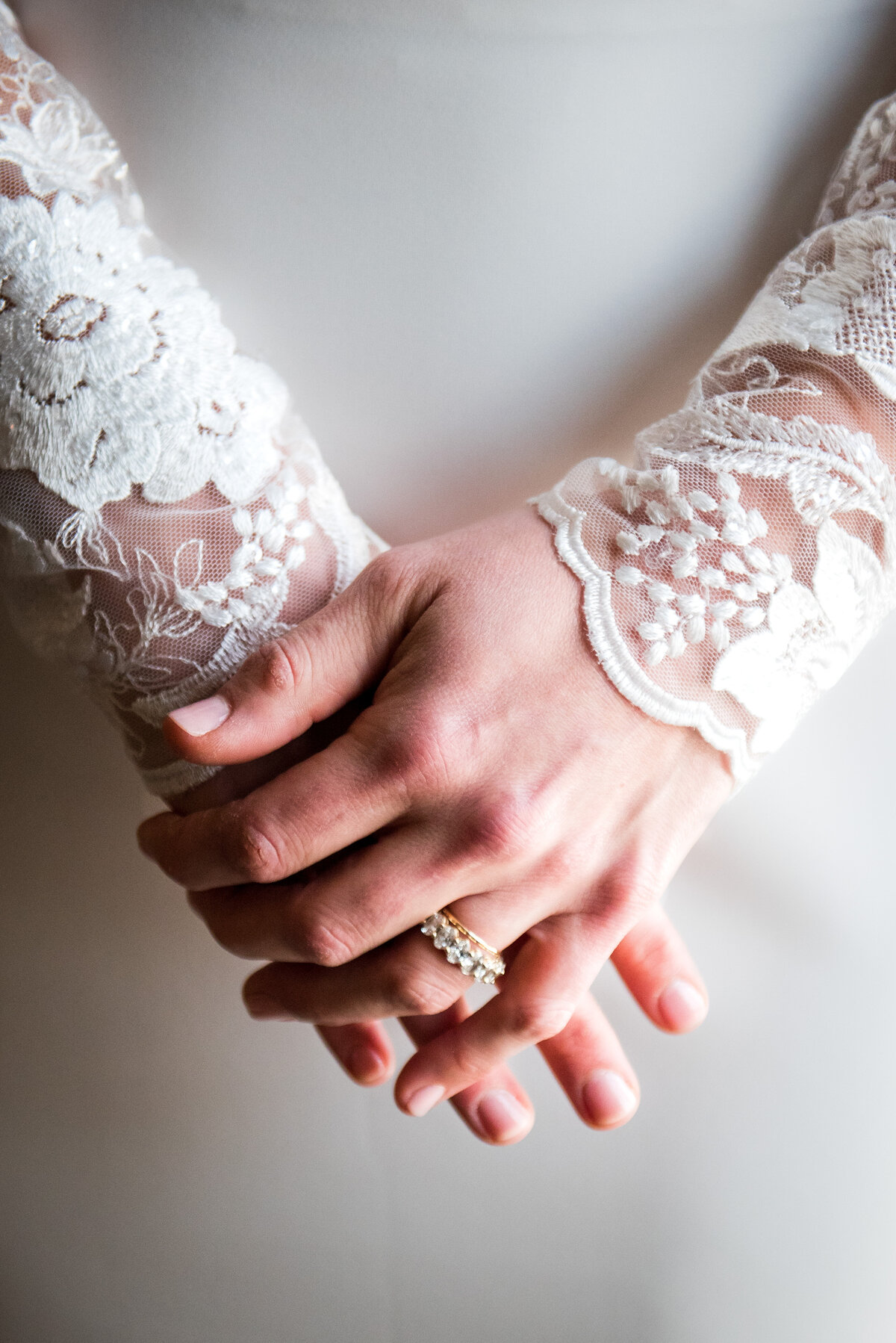 A close up shot of a bride's hands, showing her wedding rings and lacy wedding sleeves.