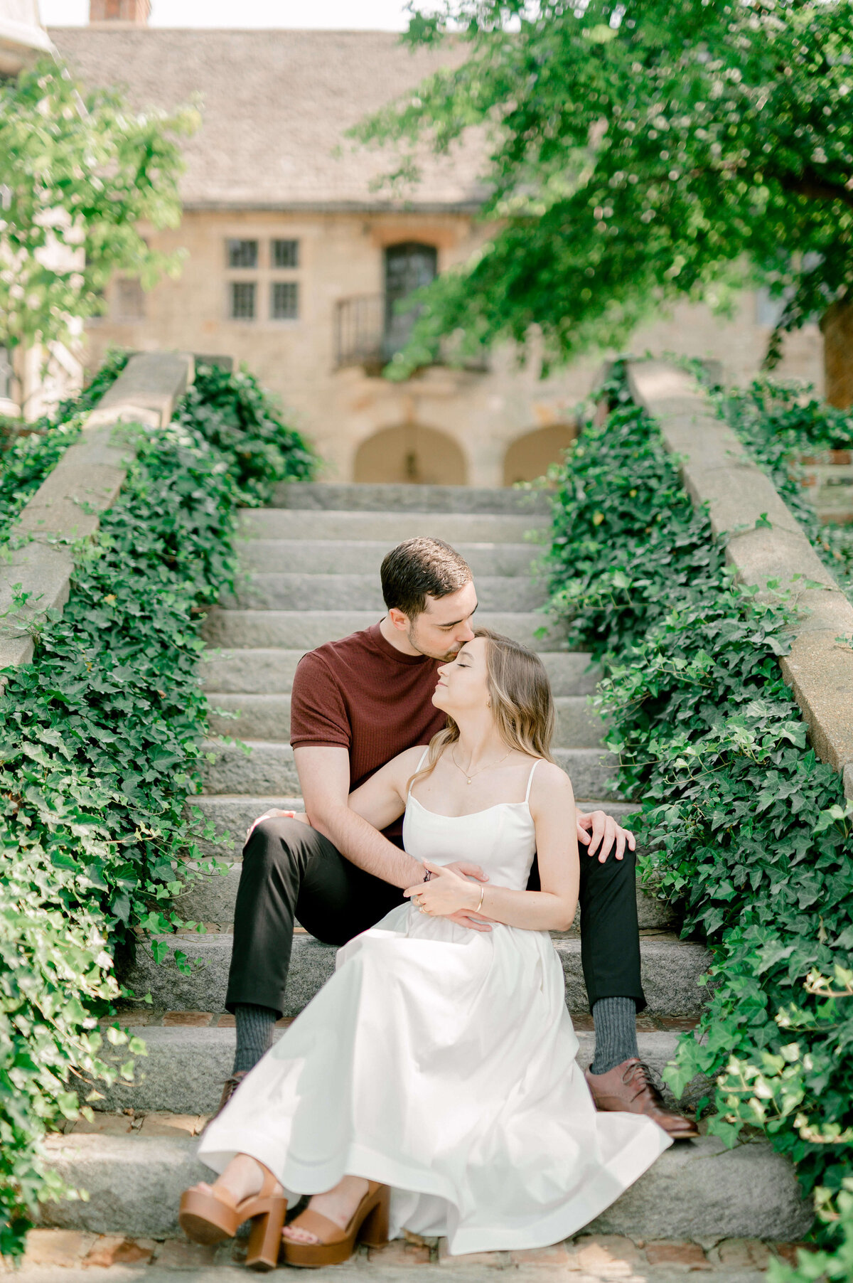 Engagement photo of a couple sitting on the ivy covered steps located in the National Cathedral Gardens