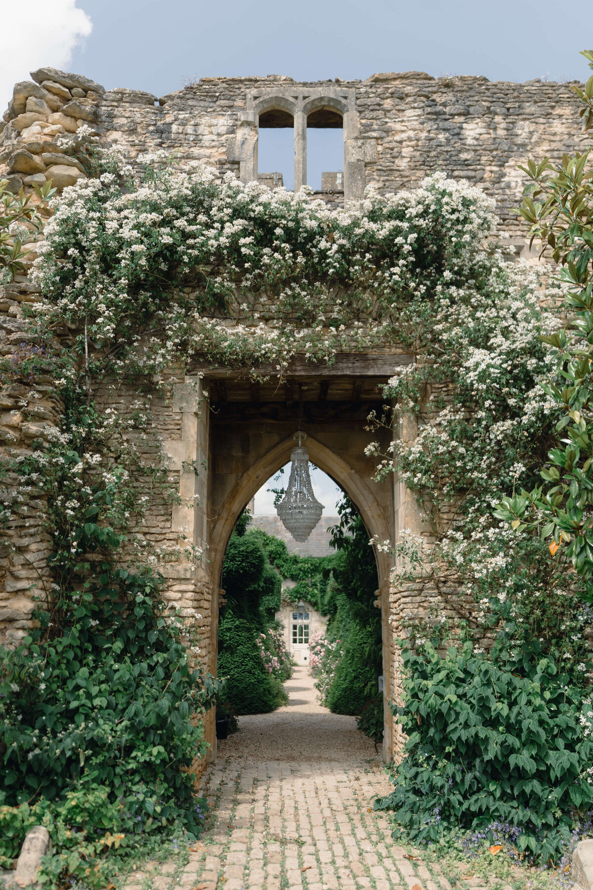 white and green flowers growing over ruins archway with chandelier hanging in the middle at cotswold wedding venue euridge manor
