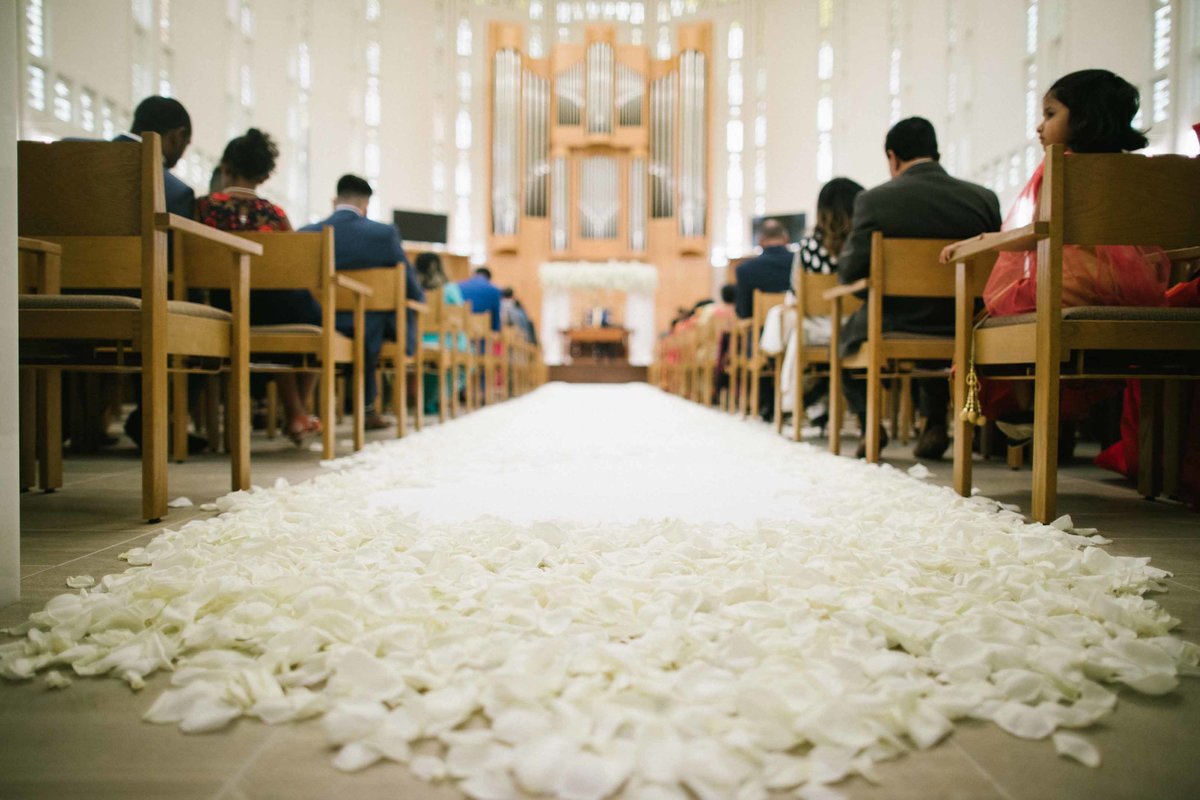 White aisle runner covered in rose petals for church wedding ceremony