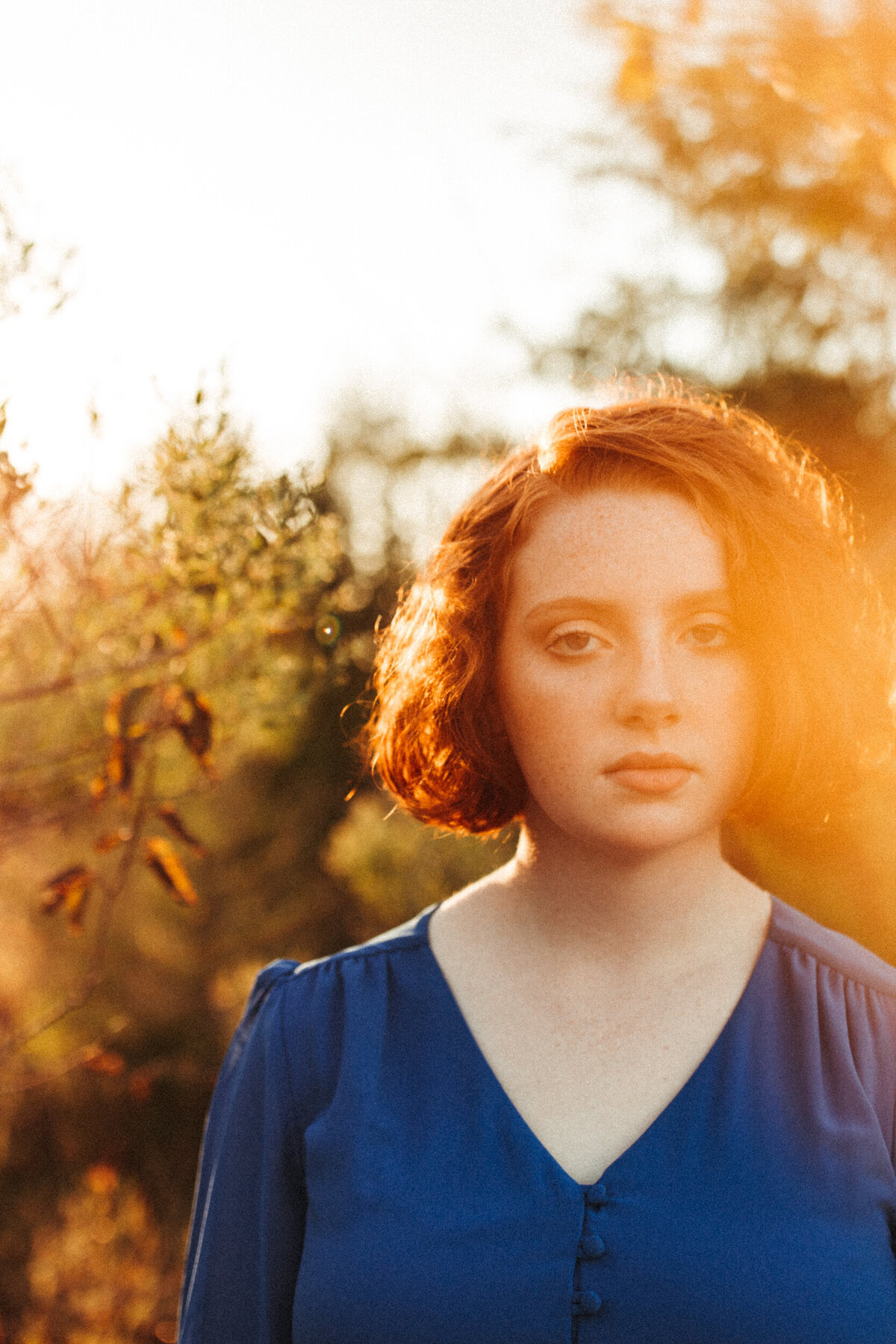 High school senior girl with short red hair and blue dress making a serious face at sunset