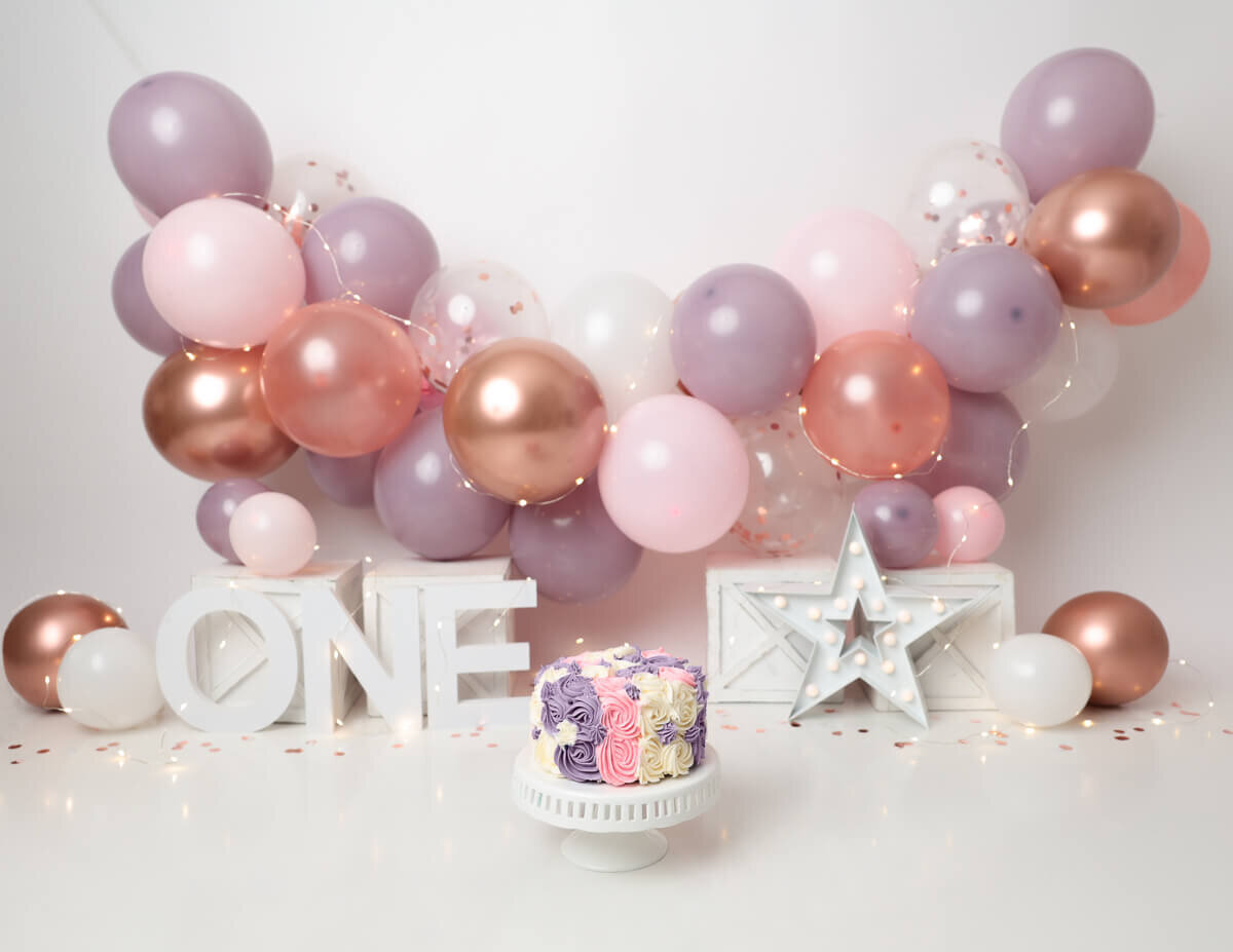 A cake smash experience in Rochester, NY featuring a pink and purple ballon garland.