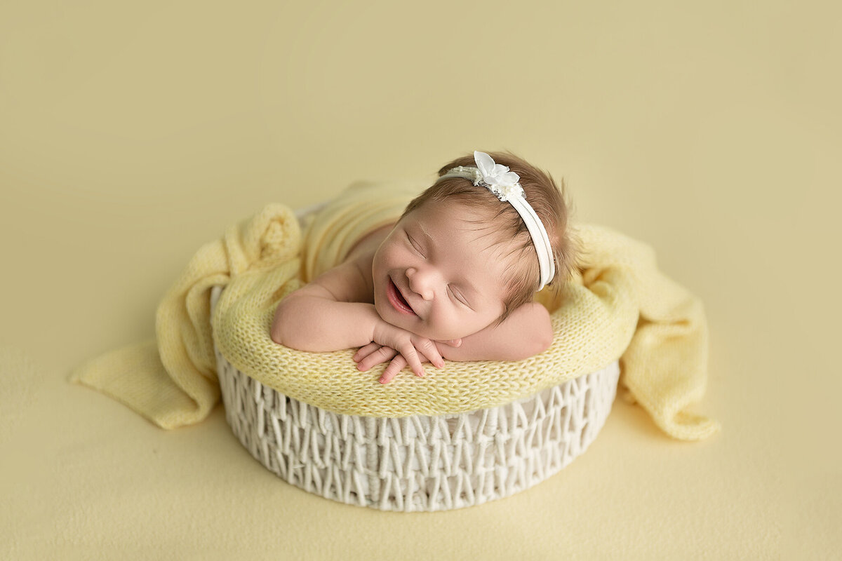 smiling-newborn-baby-girl-in-white-woven-prop-with-yellow-and-white-accents-amanda-estep-photography