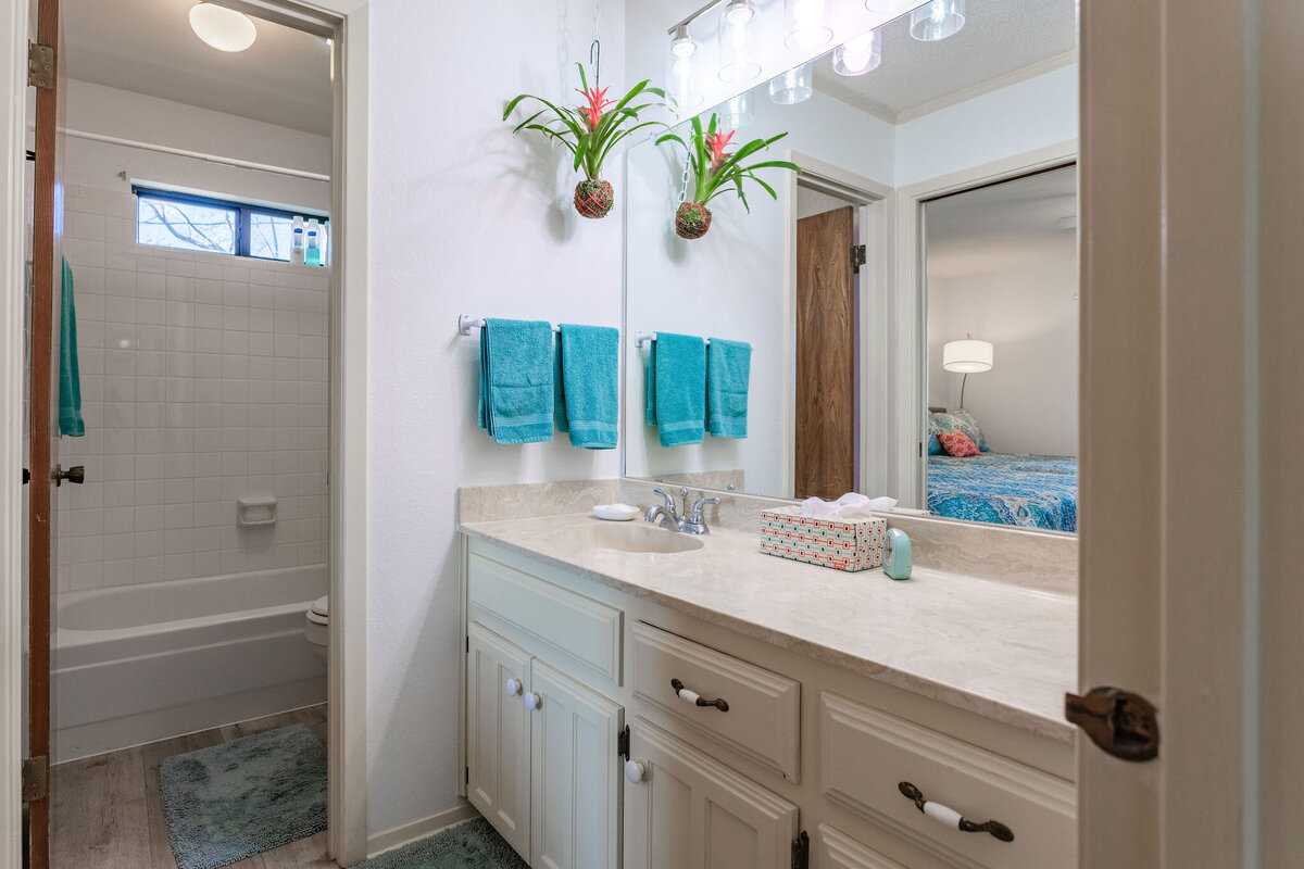 Bathroom with large mirror and plenty of lighting in this 2-bedroom, 2-bathroom lakeside vacation rental home for 6 guests on Tradinghouse Lake with privacy access to a fishing dock and boat launch pad, ping pong table, gazebo, free wifi and free parking in Waco, TX.