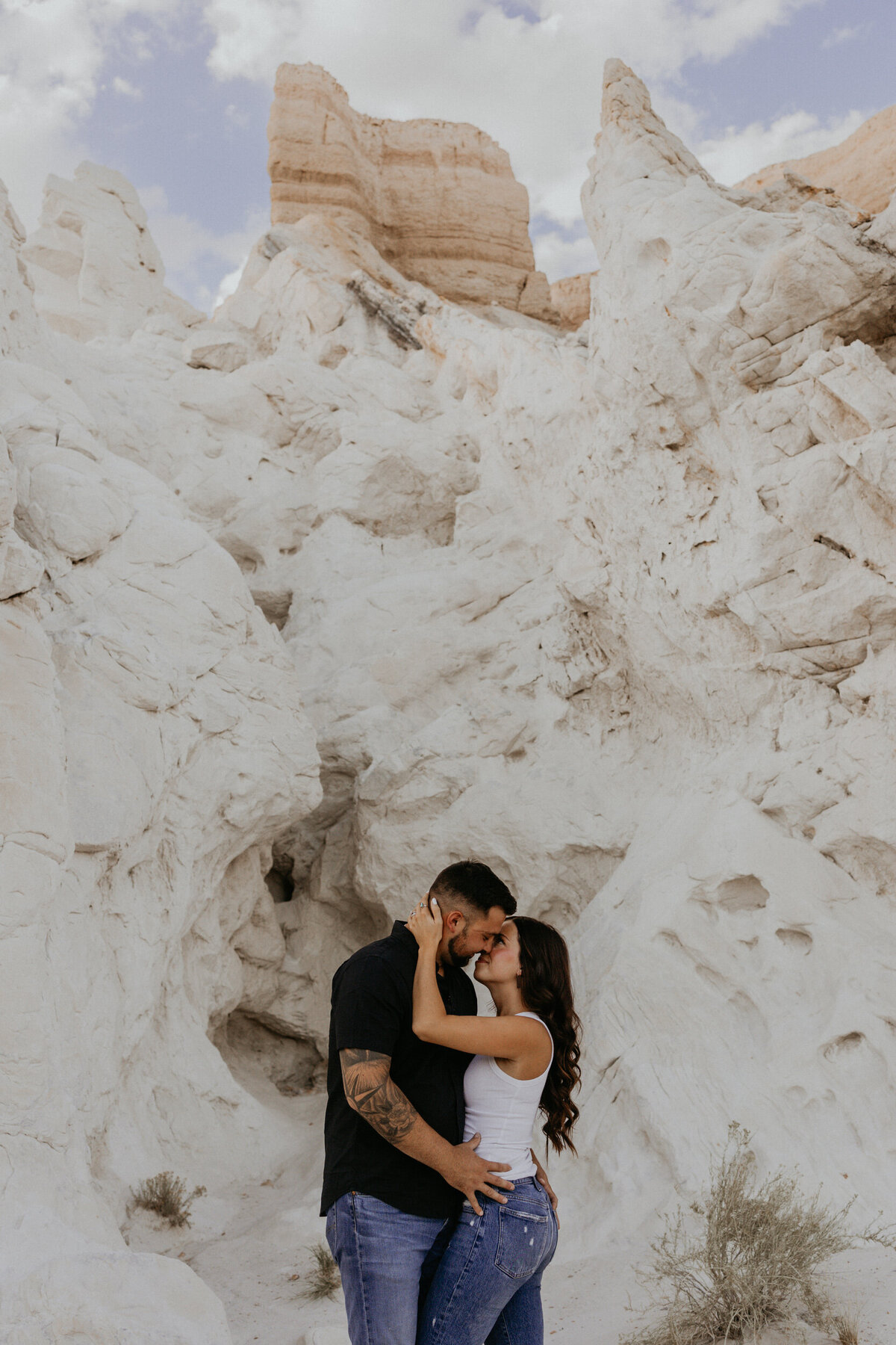 engaged couple kissing in front of a white rock in the desert