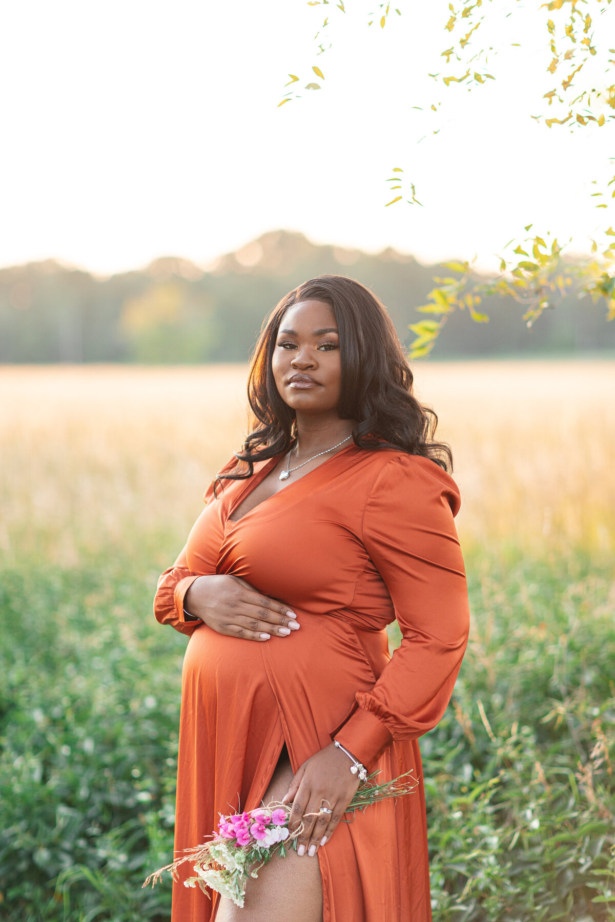 Maternity session during golden hour surrounded by grassy fields.