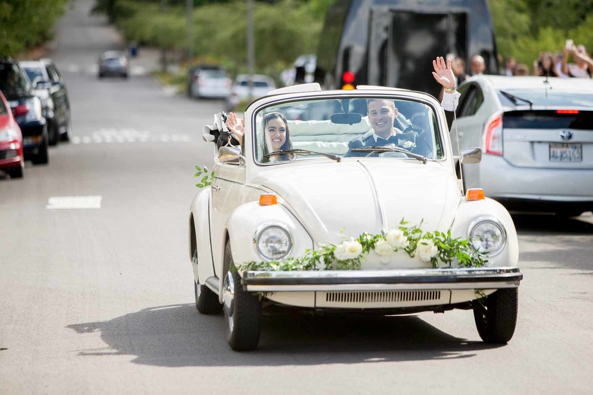 Newly weds in vintage get-away car decorated with white flowers