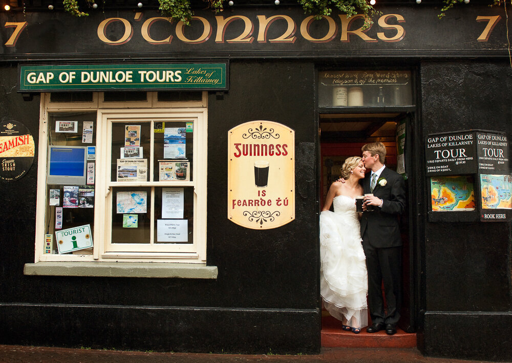 bride wearing a tulle ballroom dress kissing her groom with a black suit in the doorway of O'Connors pub, Killarney