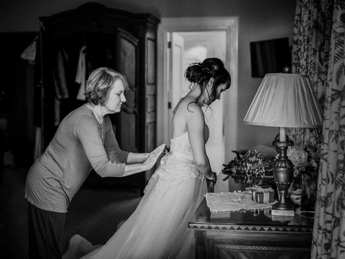 A woman helping a bride zip up her dress.