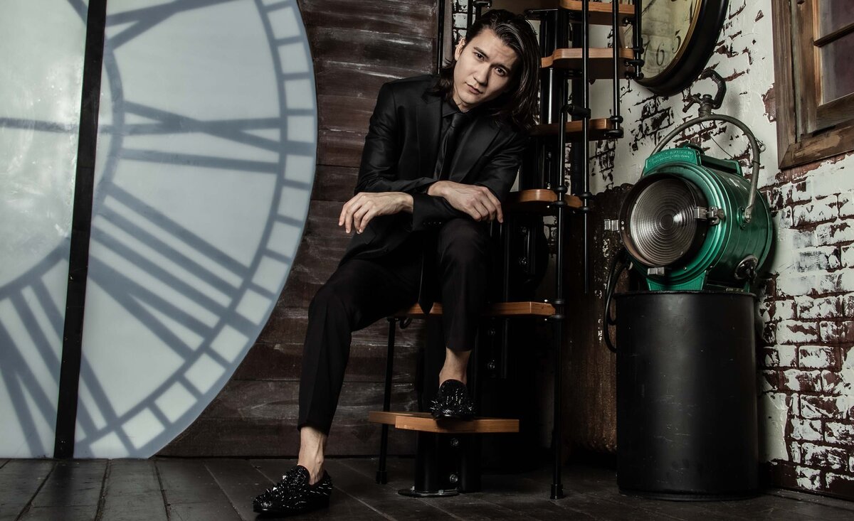 Classical musician portrait Sean Harper wearing black suit sitting against spiral stair case large clock background