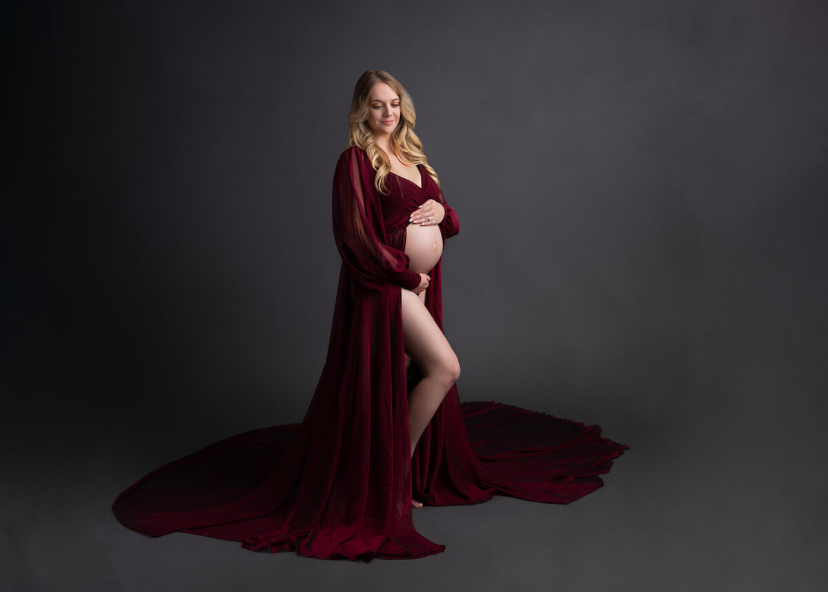 prenant woman cradling her belly posing in a maroon flowy dress